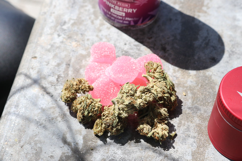 Cannabis buds beside pink gummy candies on a stone surface